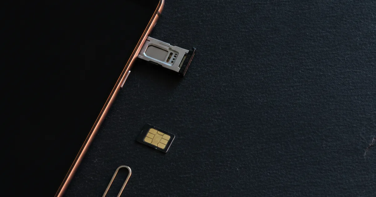 Bandeja del SIM medio sacada de un celular apoyado sobre pizarra oscura, con el pin expulsor y la tarjeta nano-SIM al lado